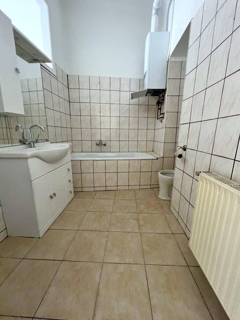 Badezimmer mit Badewanne, Waschbecken und Fliesen an Wänden und Boden.