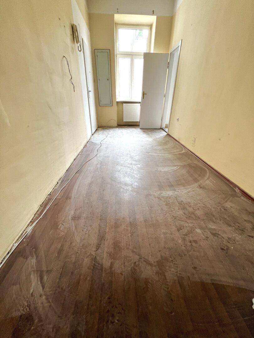 Langer, leerer Raum mit Holzboden und gelben Wänden, bereit zur Renovierung.