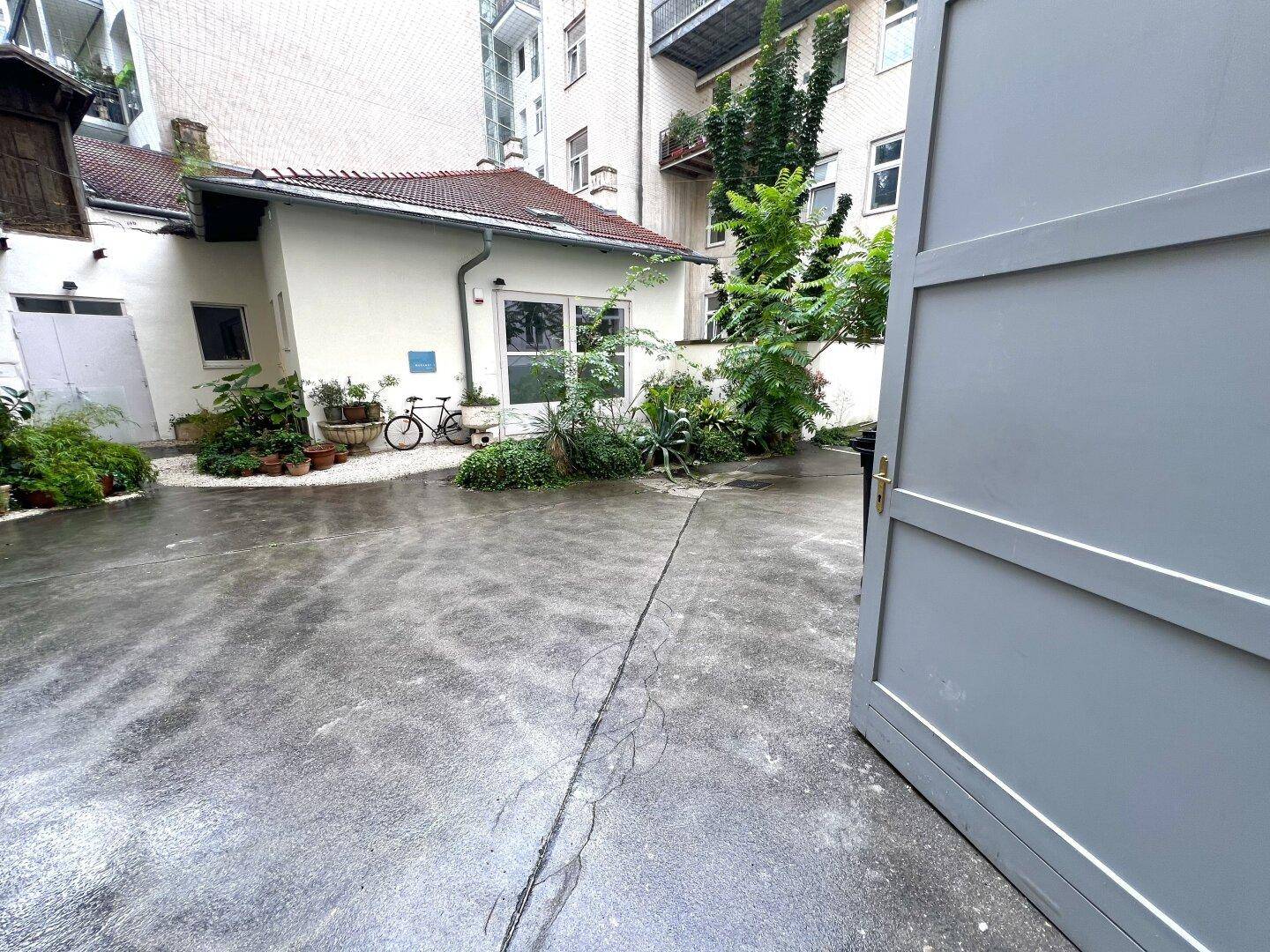 Gepflasterter Innenhof mit Pflanzen und einem Fahrrad, umgeben von Gebäuden.