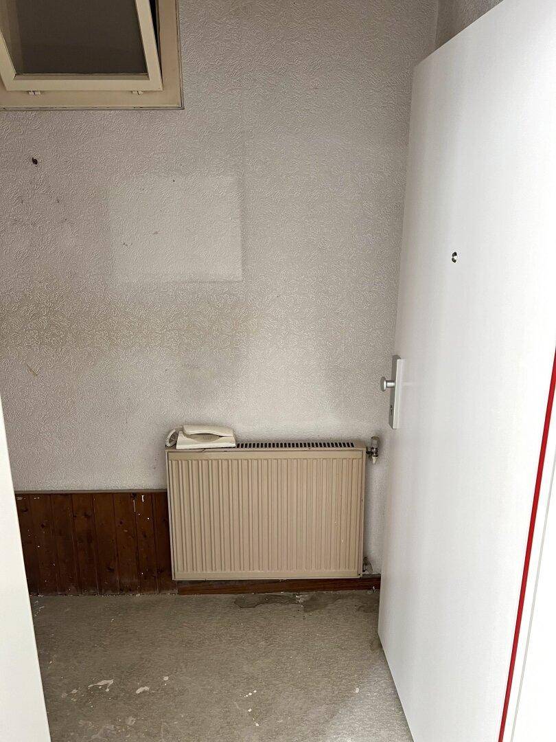 Eingangsbereich mit Heizkörper und einfacher Tür, der auf eine Renovierung wartet.