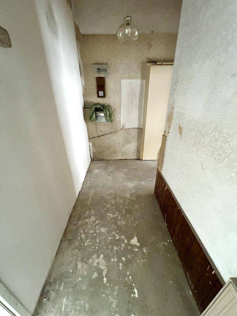 Schmaler Flur in sanierungsbedürftigem Zustand mit abgenutztem Boden und teilweise entfernter Wandverkleidung.