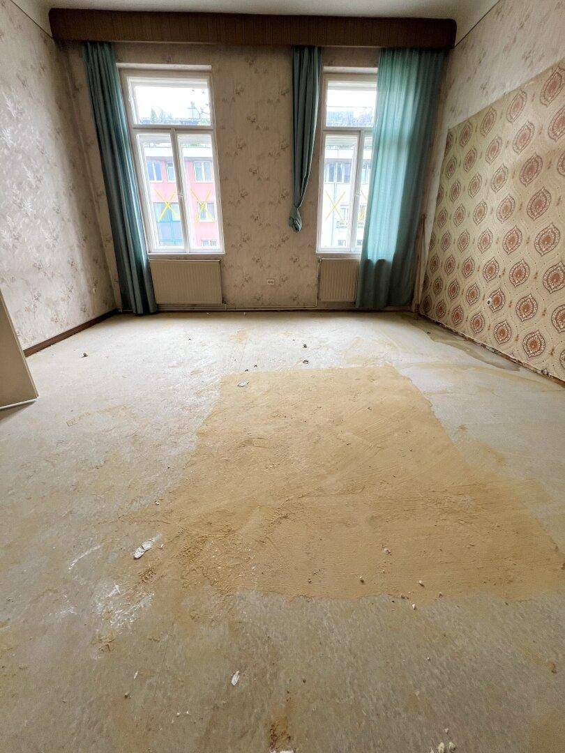 Unrenoviertes Schlafzimmer mit abgenutztem Teppichboden und alter Tapete, bereit zur Sanierung.