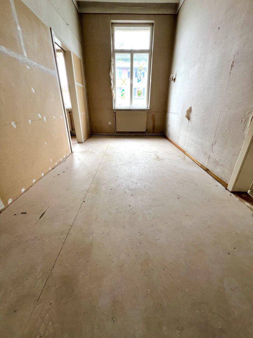 Leerer Raum in Renovierung mit kahlen Wänden und einem Fenster, das Tageslicht hereinlässt.