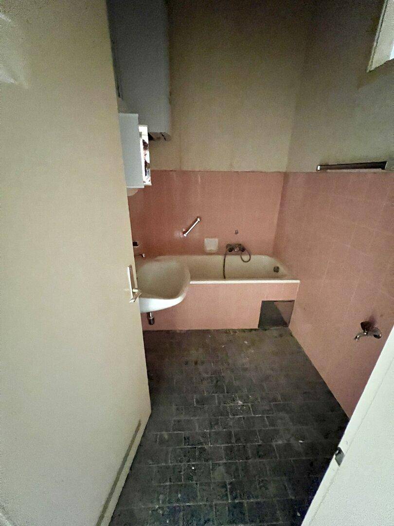 Veraltetes Badezimmer mit rosa Fliesen, Badewanne und Waschbecken, das eine Modernisierung benötigt.