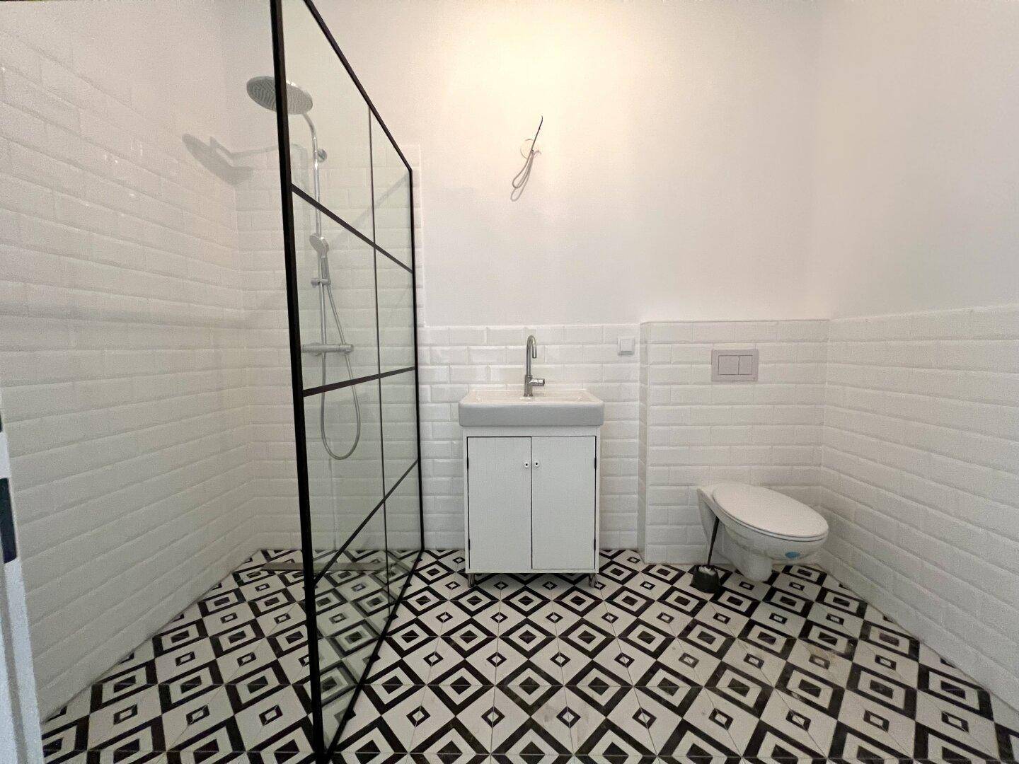 Helles Badezimmer mit modernen schwarz-weißen Fliesen, Dusche und wandhängendem WC.
