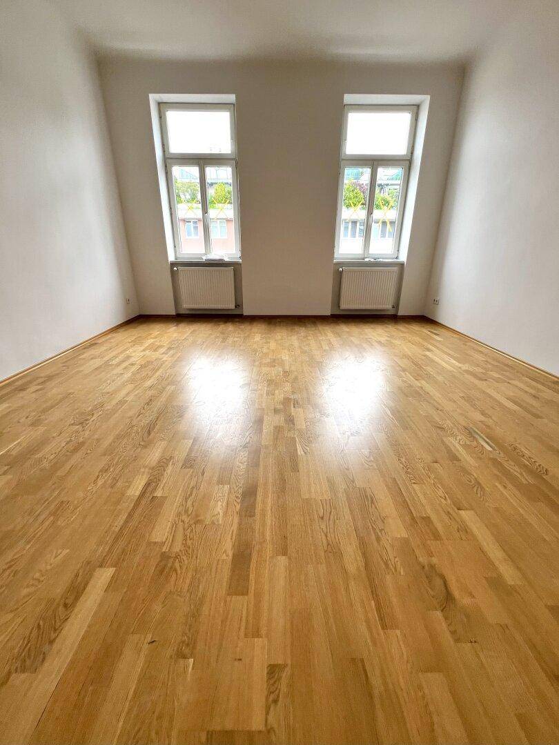 Helles Zimmer mit Holzboden und zwei Fenstern, ideal als Wohn- oder Schlafzimmer im Dachgeschoss.