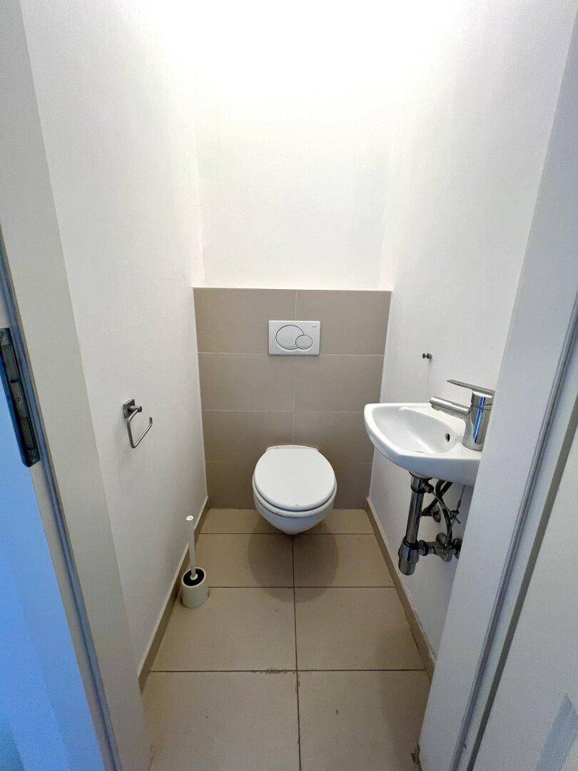 Separates WC mit Wand-WC, kleinem Waschbecken und beigefarbenen Fliesen.