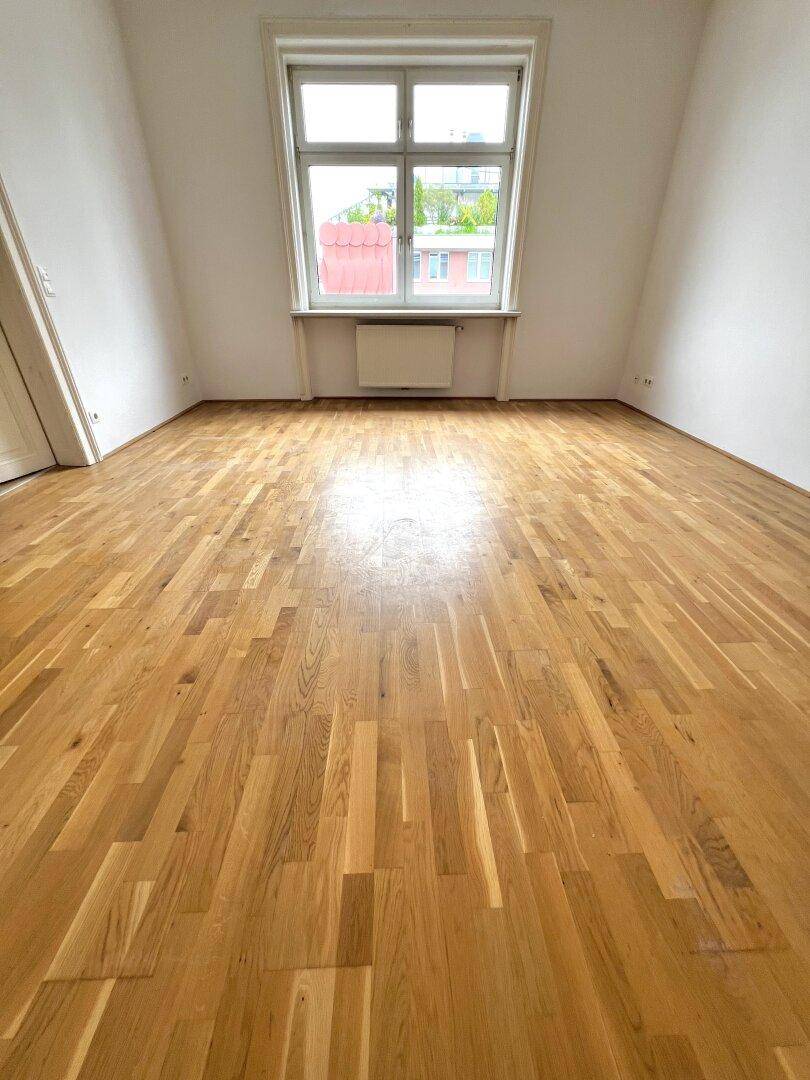 Geräumiges Zimmer mit hellem Parkettboden und Fenster, bietet vielseitige Nutzungsmöglichkeiten.