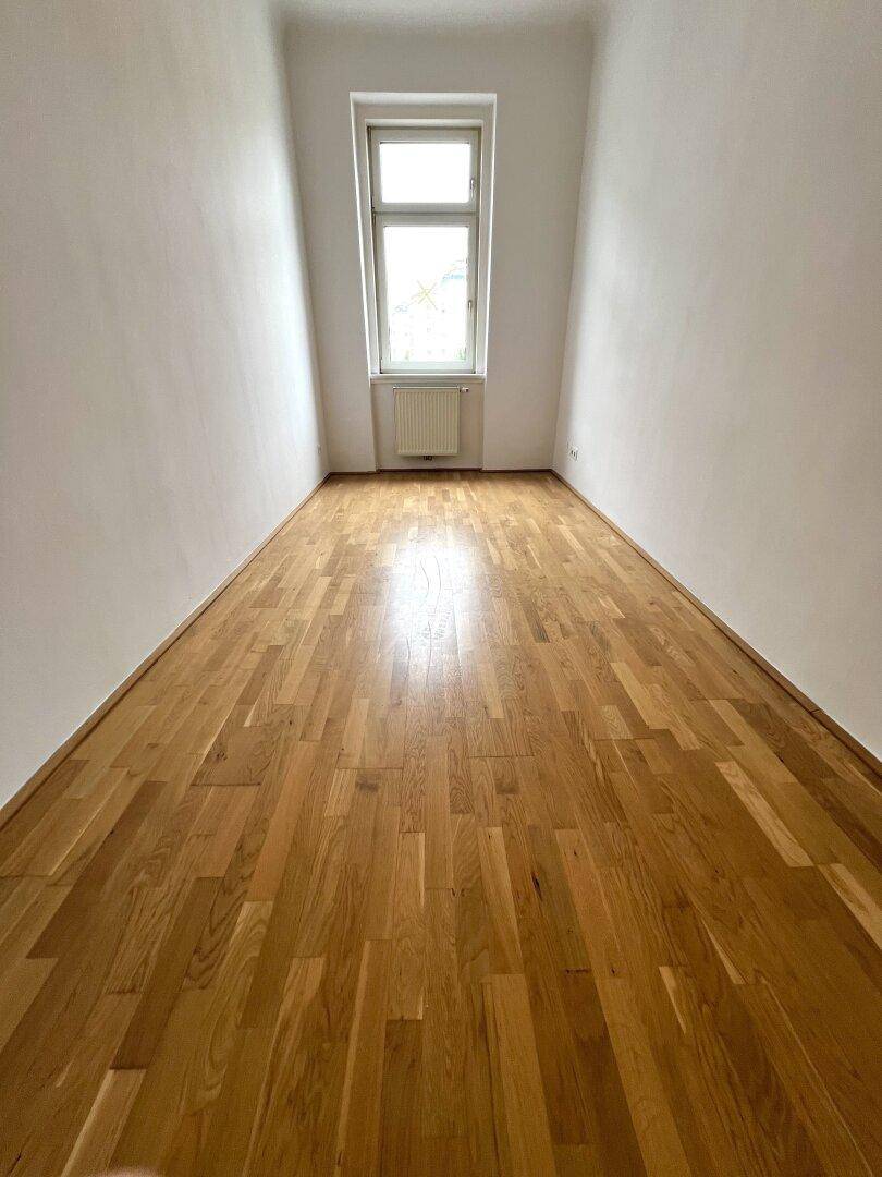 Langes, helles Zimmer mit Parkettboden und Fenster, vielseitig nutzbar.