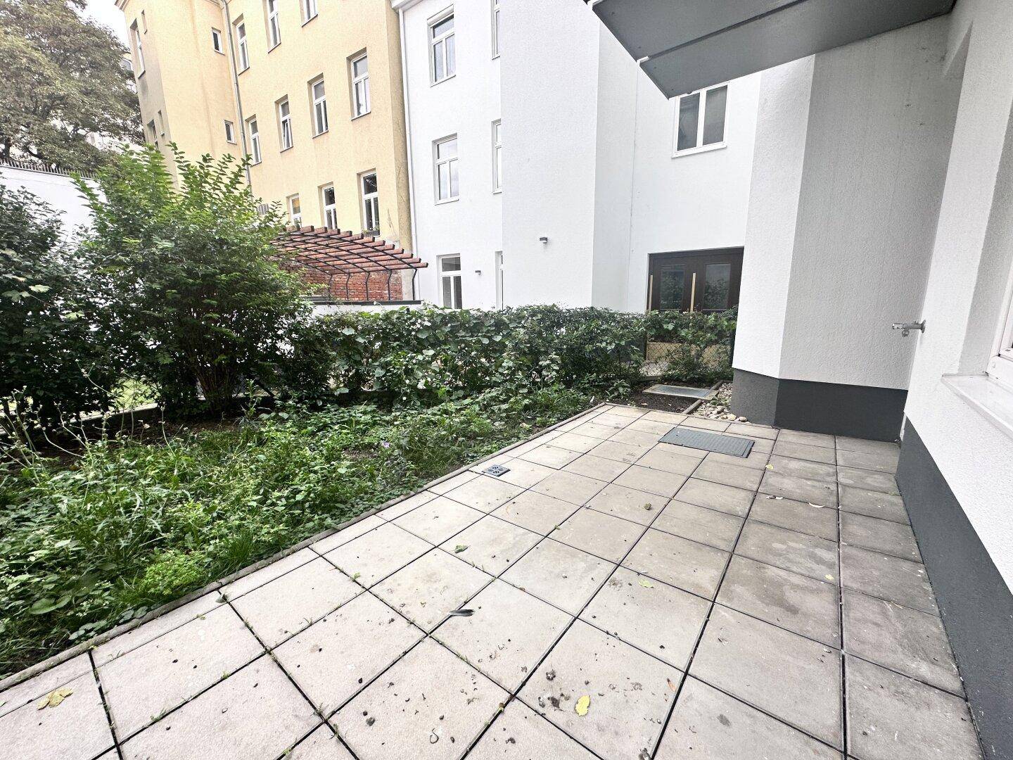 Gepflasterte Terrasse mit angrenzendem Gartenbereich und Blick auf die umliegenden Gebäude.