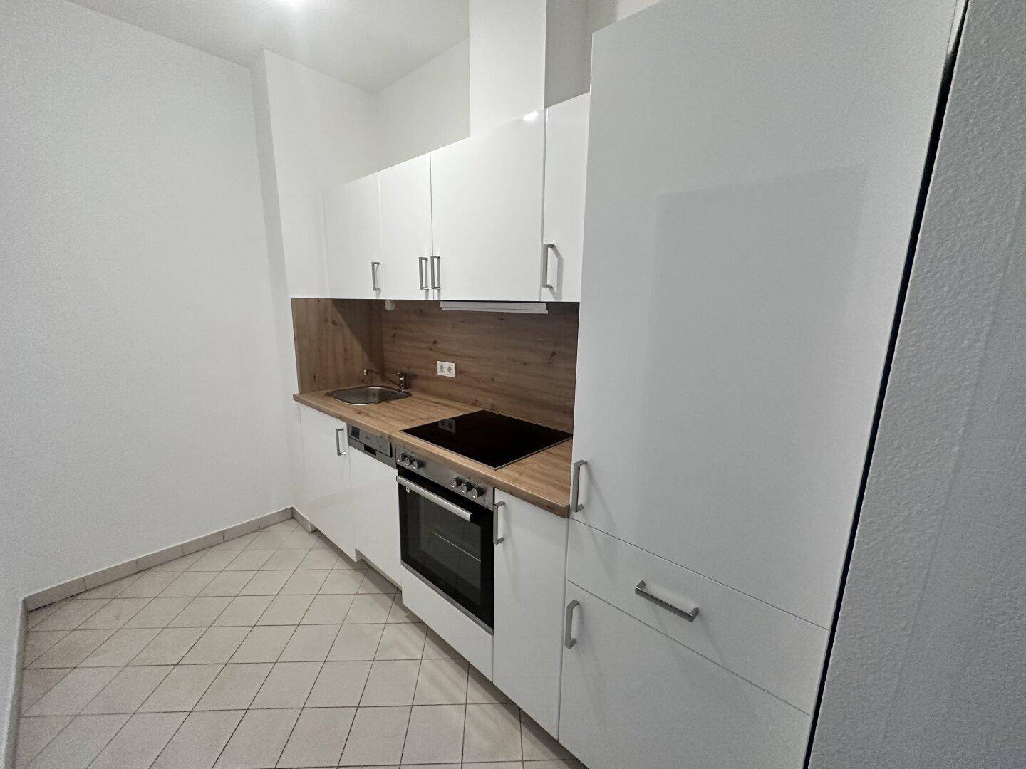 Moderne Einbauküche mit weißen Hochglanzfronten, Induktionskochfeld und Holzoptik-Arbeitsplatte.
