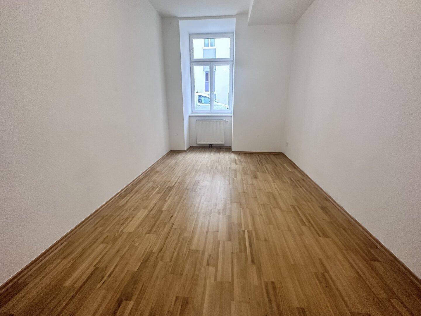 Kleiner, heller Raum mit Parkettboden und einem Fenster, geeignet als Schlaf- oder Arbeitszimmer.