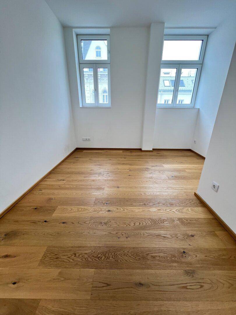 Heller, leerer Raum mit hochwertigem Holzboden und Dachschrägenfenstern, ideal als Wohn- oder Schlafzimmer.