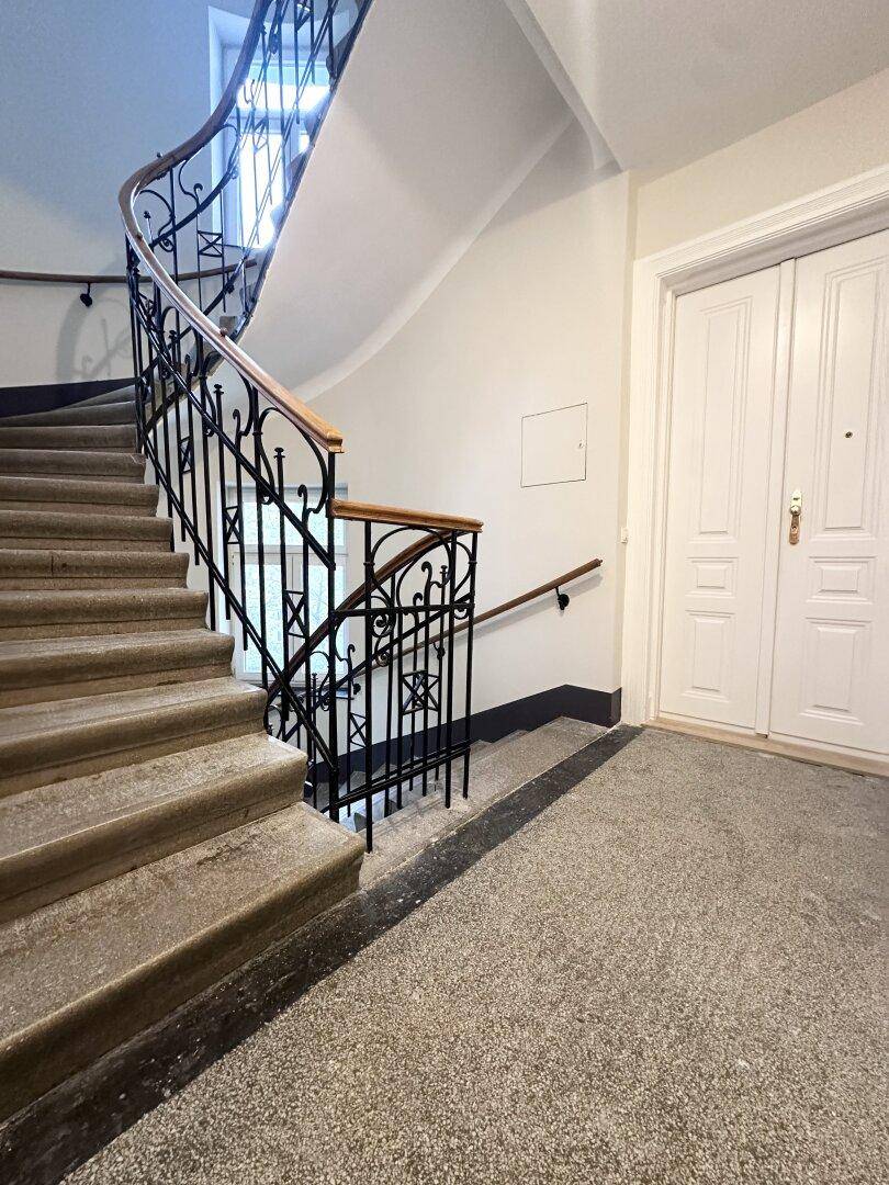 Historisches Treppenhaus mit schmiedeeisernem Geländer und Steinstufen in einem Altbau.