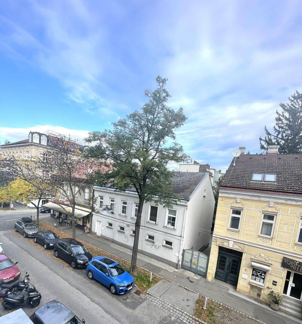 Blick auf eine belebte Straße mit parkenden Autos und umliegenden Gebäuden unter blauem Himmel.