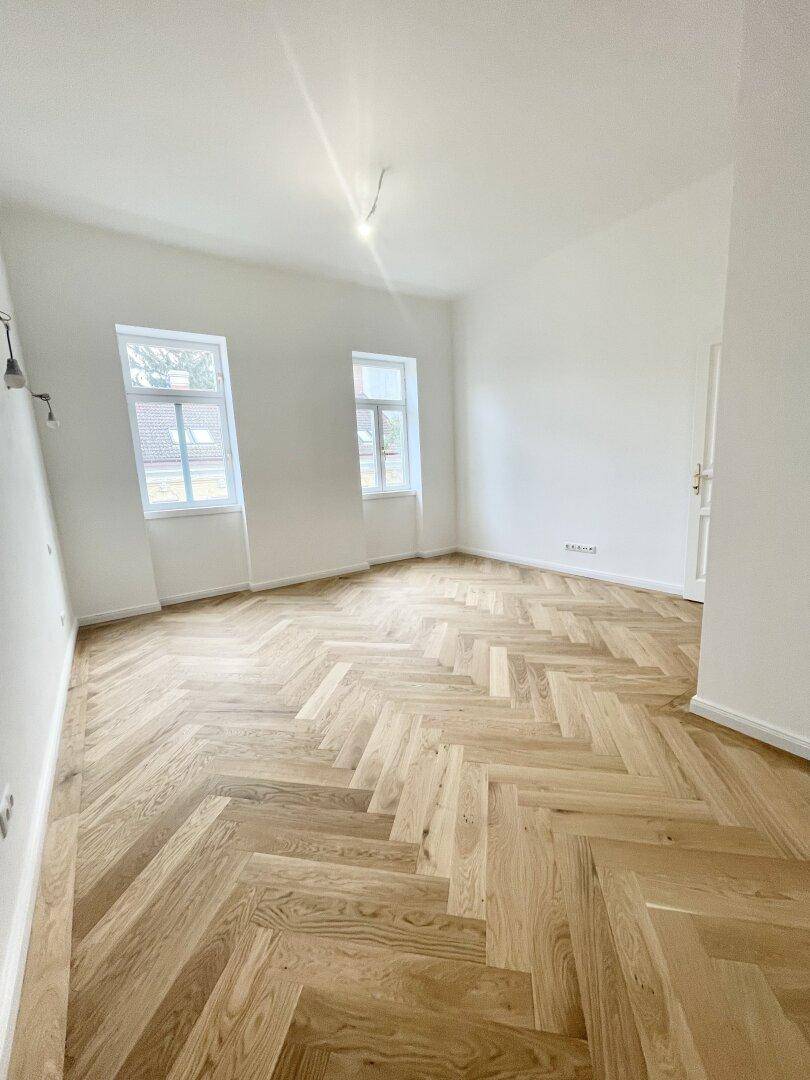 Geräumiges Zimmer mit elegantem Fischgrätparkett und weißen Wänden, bietet viel Gestaltungspotenzial.