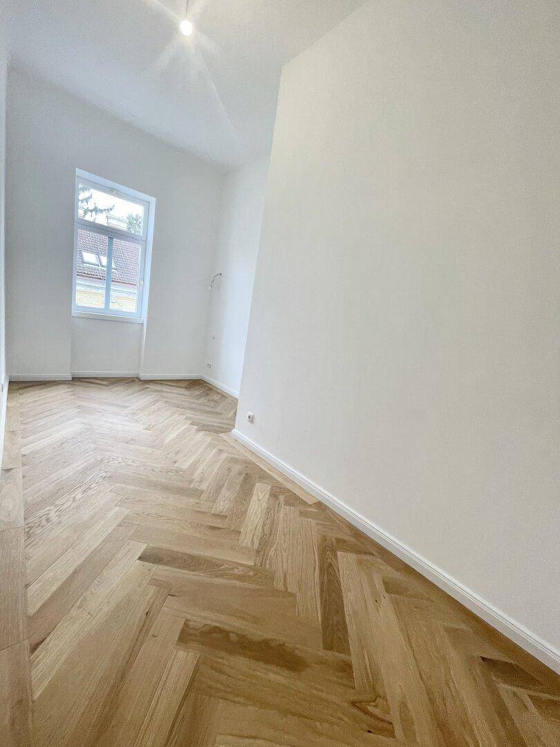 Langer, heller Raum mit Fischgrätparkett und einem Fenster, ideal als Flur oder Arbeitsbereich.