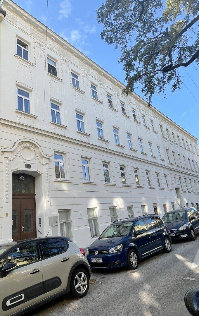 Weißes Altbaugebäude mit klassischer Fassade und parkenden Autos auf der Straße.