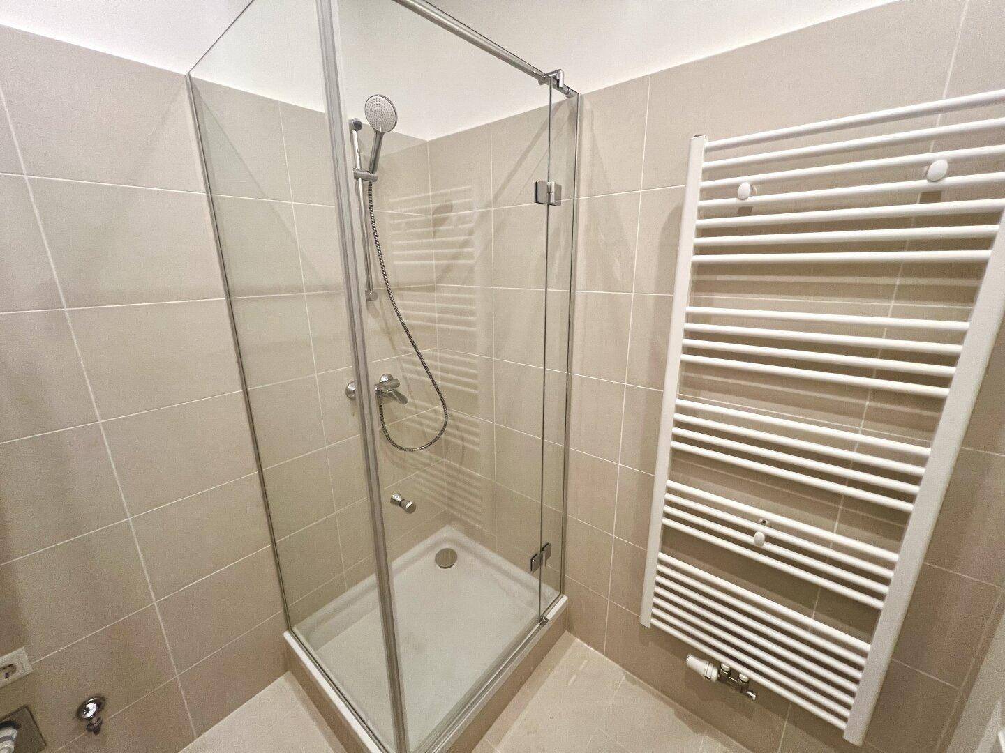 Modernes Badezimmer mit Duschkabine aus Glas, beigefarbenen Fliesen und beheiztem Handtuchhalter.