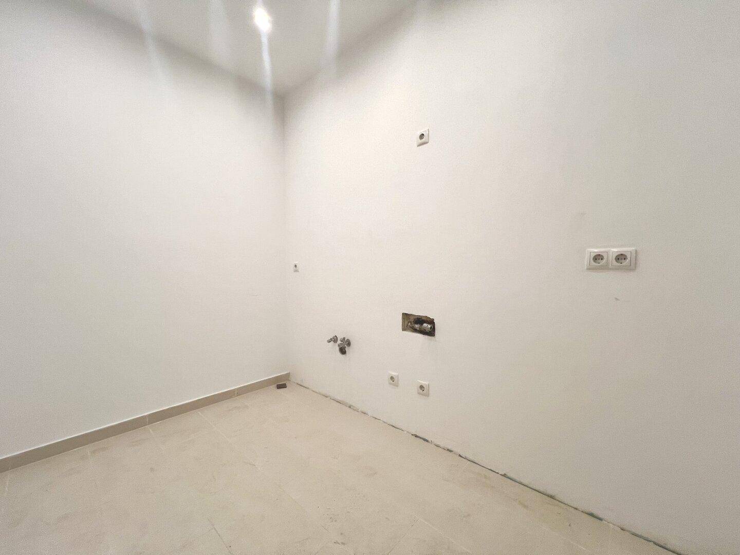 Unfertiger Raum mit sichtbaren Anschlüssen für Wasser und Strom, bereit für die Kücheninstallation.