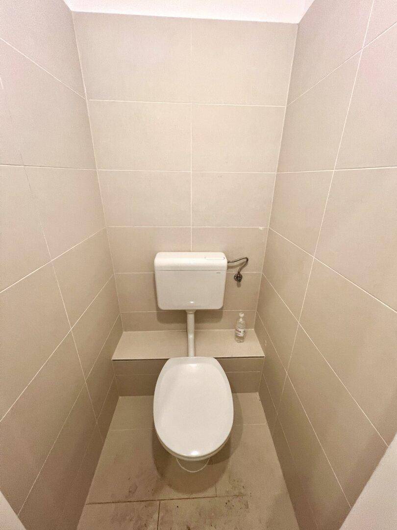 Kompaktes Gäste-WC mit beigefarbenen Fliesen und einer einfachen Toilette, funktional und sauber.