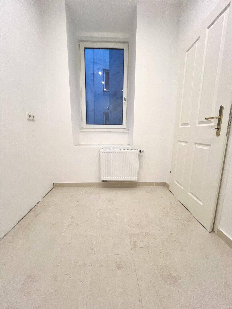 Helles Zimmer mit Fliesenboden und einem Fenster, das viel Tageslicht hereinlässt.
