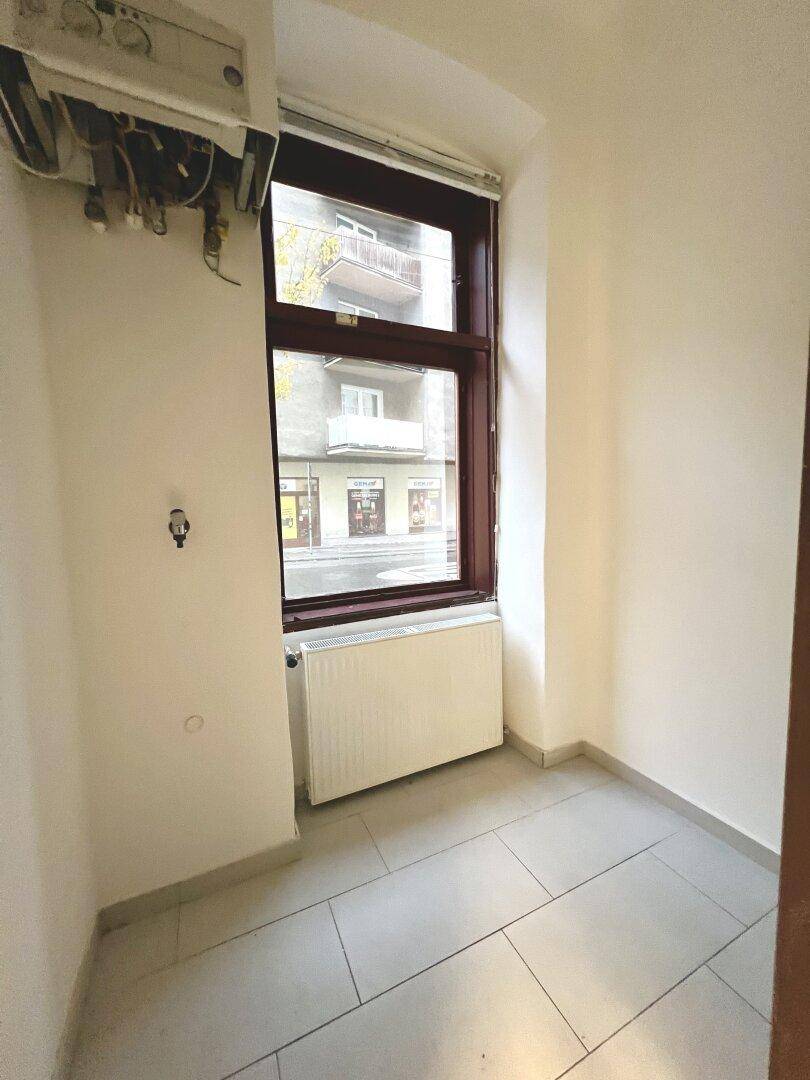 Kleiner Raum mit Fenster, Heizkörper und sichtbarem Warmwasserbereiter, ideal als Abstellraum.