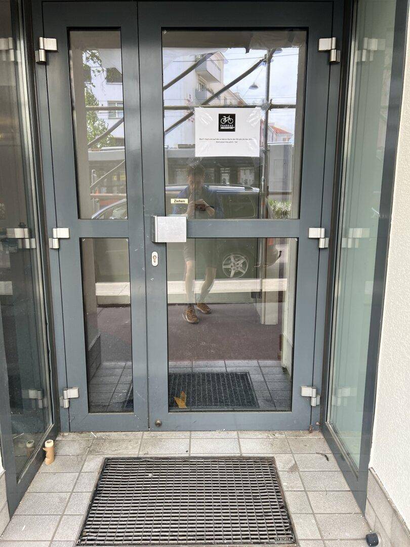 Graue Glastür als Haupteingang des Gebäudes mit Fliesenboden und Fußmatte.