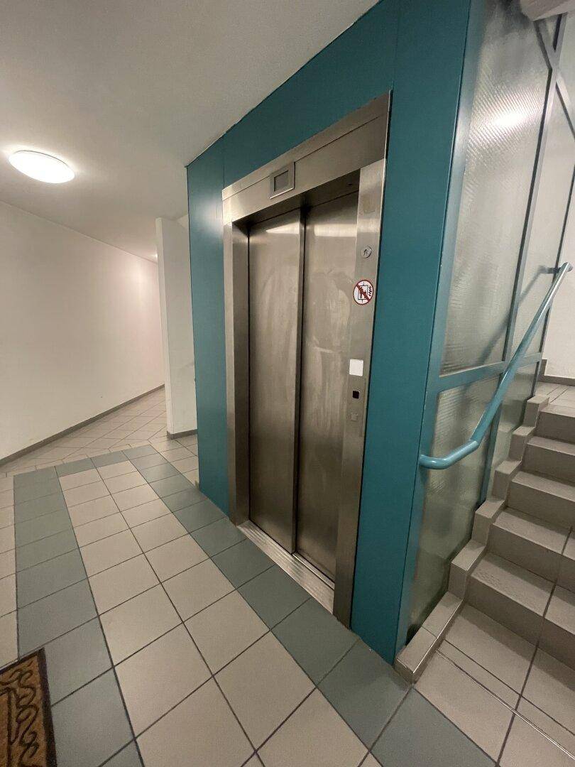 Gemeinschaftsflur mit Aufzug, Treppenhaus und Fliesenboden.