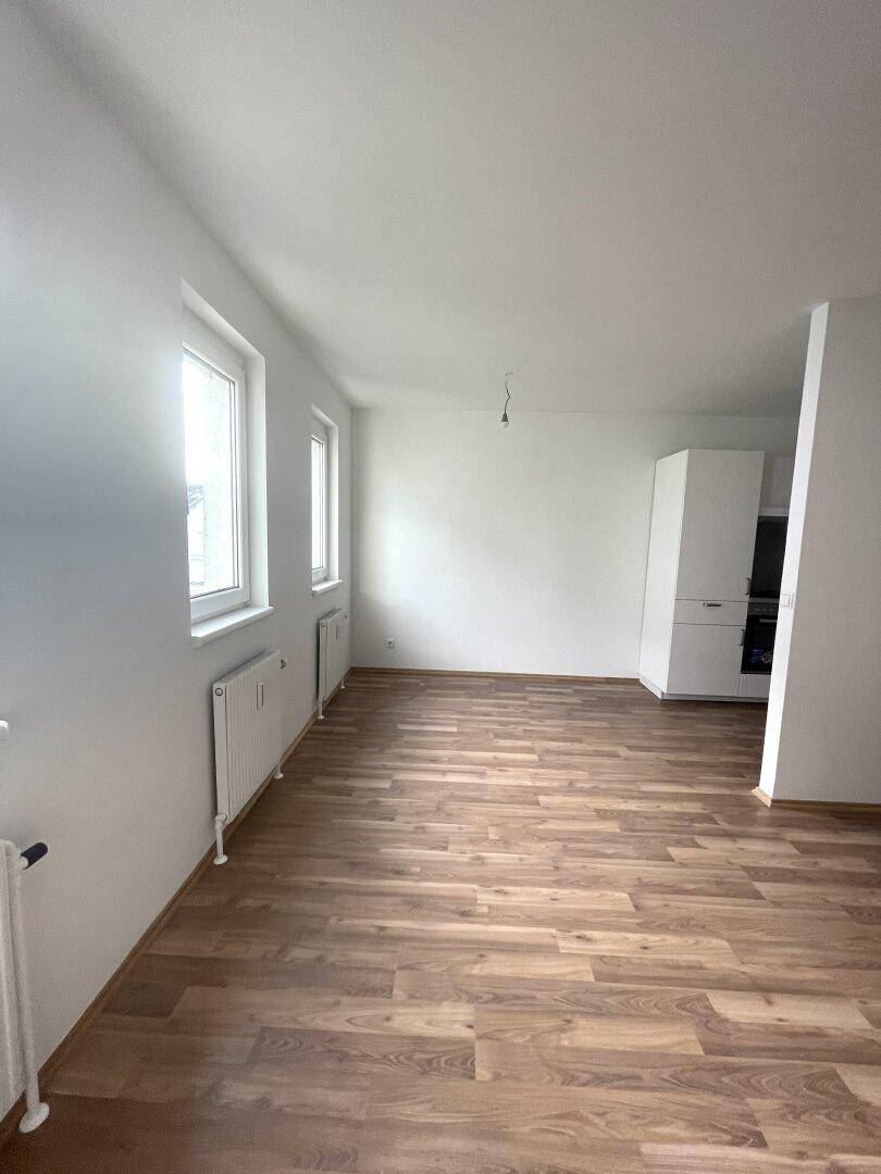 Heller Wohnbereich mit Laminatboden, weißen Wänden und Blick auf die Küchenzeile.