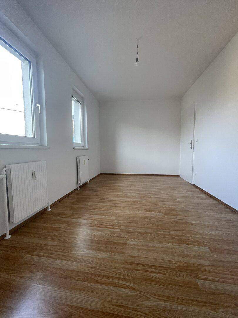 Helles Schlafzimmer mit Laminatboden, weißen Wänden und zwei Fenstern.