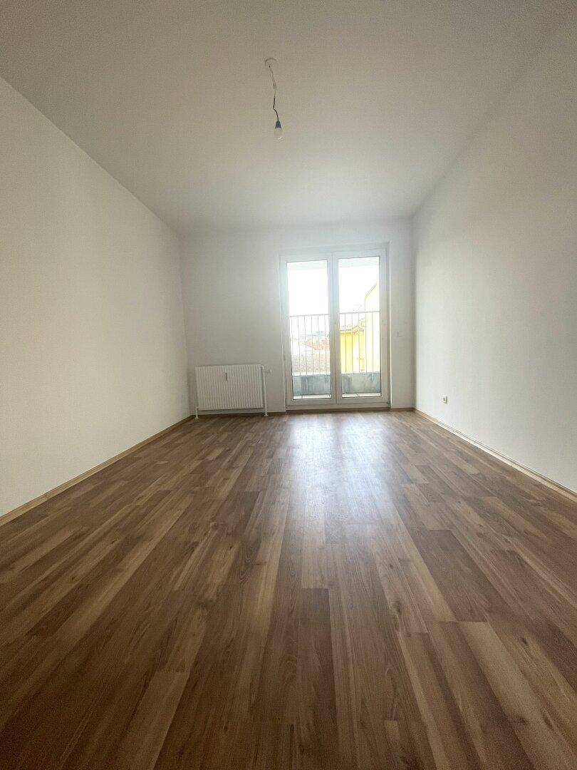 Leeres Zimmer mit Laminatboden und Zugang zu einem französischen Balkon.