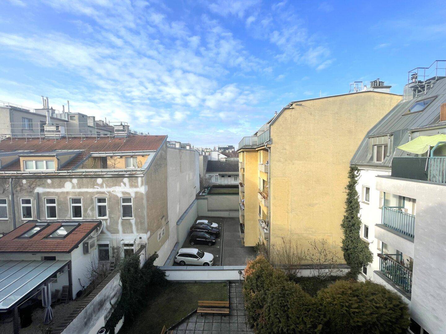 Blick auf einen Innenhof mit Parkplätzen, Grünflächen und umliegenden Gebäuden.