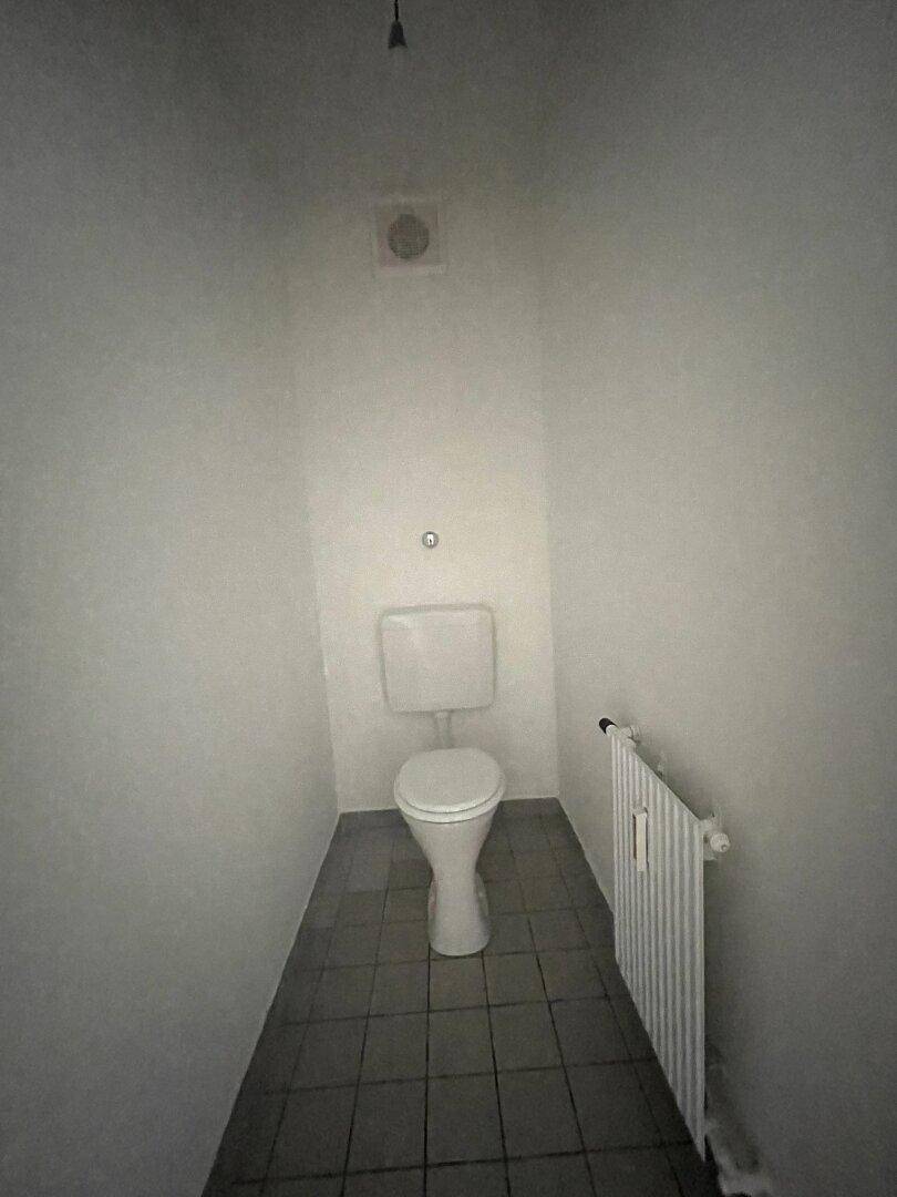 Separate Toilette mit WC, Heizkörper und Fliesenboden.