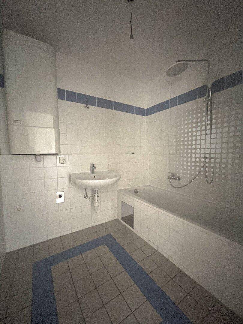 Badezimmer mit Badewanne, Waschbecken, weißen Fliesen und blauen Akzenten.