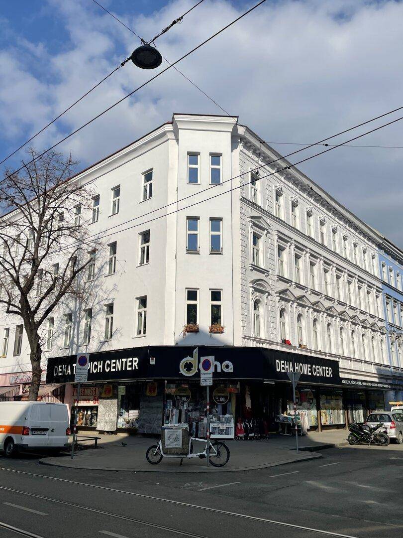 Eckgebäude mit Geschäften im Erdgeschoss und Wohnungen darüber an einer städtischen Straße.