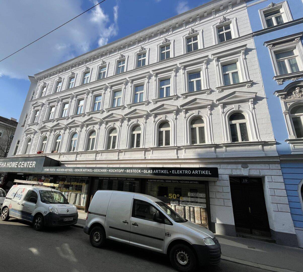 Historische Fassade eines Wohn- und Geschäftshauses mit vielen Fenstern und Verzierungen.