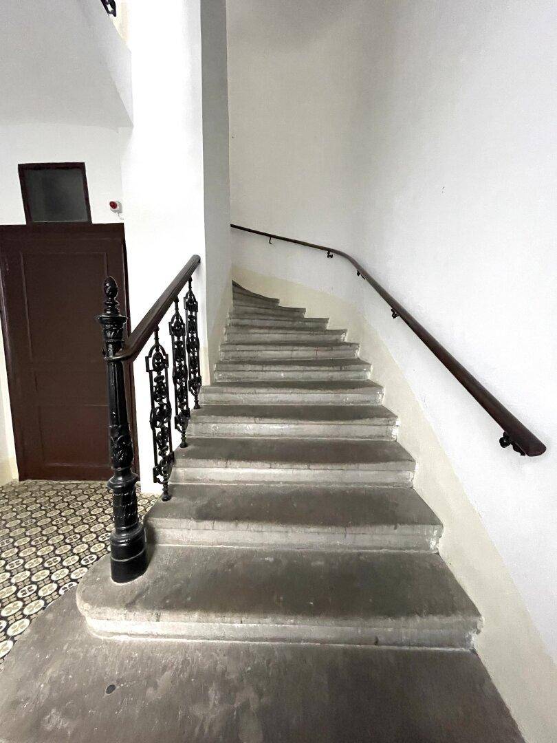 Historisches Treppenhaus mit Steinstufen und einem schmiedeeisernen Geländer in einem Altbau.
