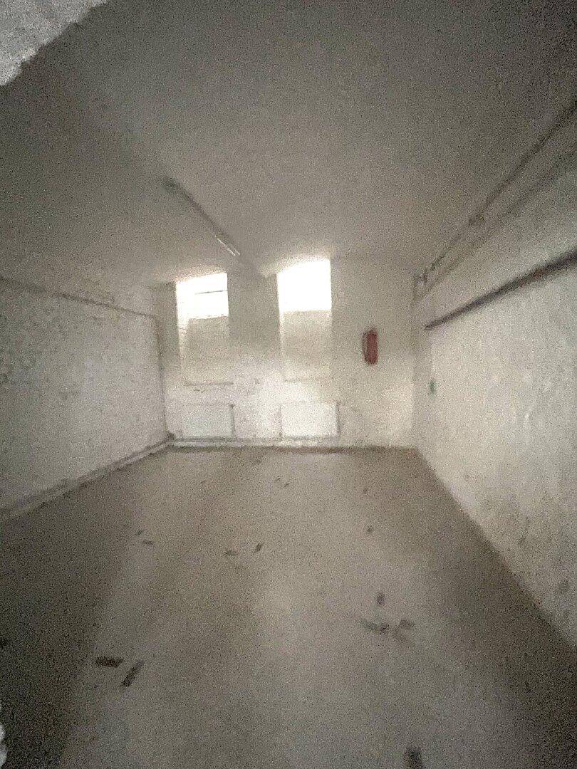 Leerer Raum mit weiß gestrichenen Ziegelwänden, Betonboden und zwei kleinen Fenstern, die Tageslicht hereinlassen.