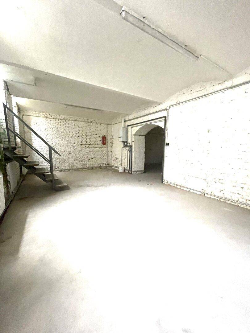 Großer Kellerraum mit weiß gestrichenen Ziegelwänden, Betontreppe und Gewölbedecke.