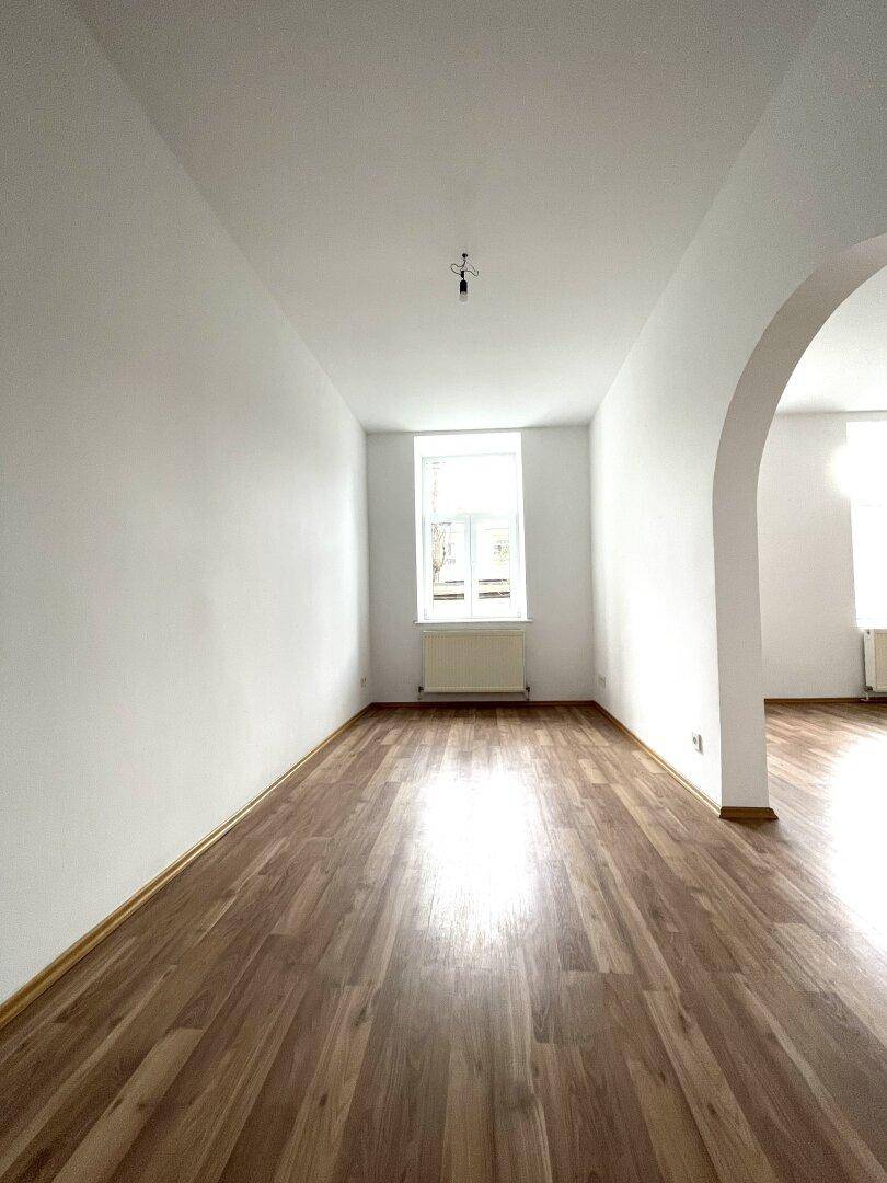 Schlafzimmer mit Laminatboden, weißen Wänden und einem Fenster, das viel Tageslicht hereinlässt.