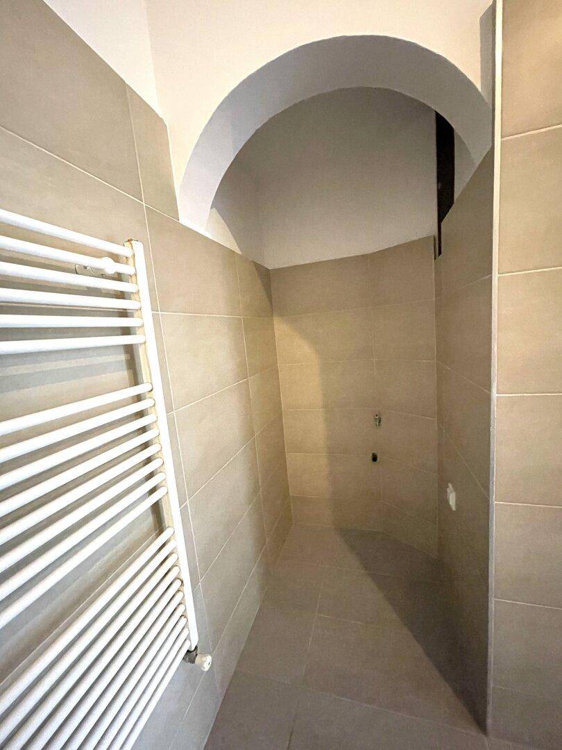Modern geflieste Dusche mit beigefarbenen Fliesen und einer gewölbten Decke.