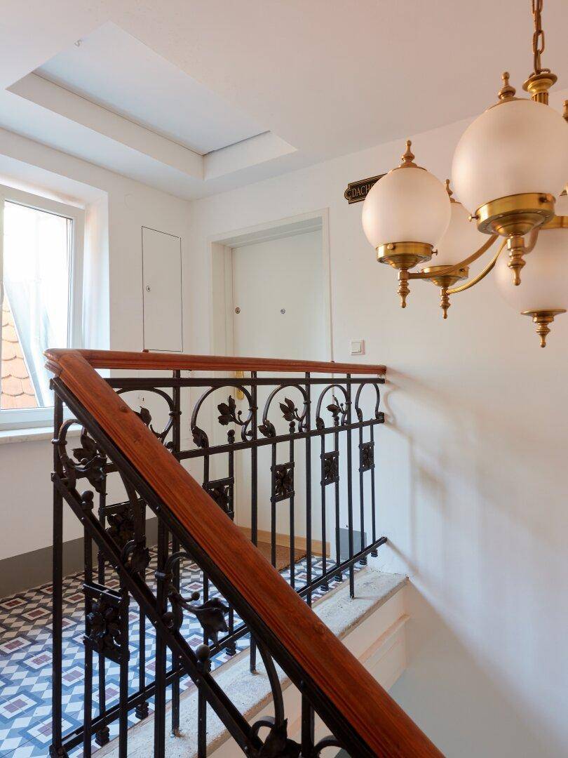 Historisches Treppenhaus mit schmiedeeisernem Geländer, Holzakzenten und gemusterten Fliesen.