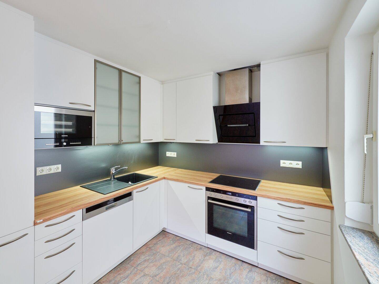 Moderne Einbauküche mit weißen Schränken, Holz-Arbeitsplatten und integrierten Geräten.