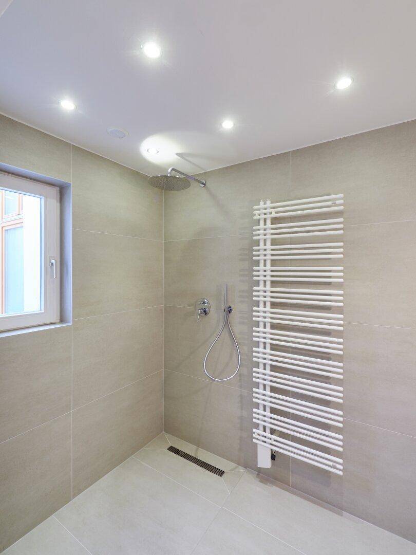 Modernes Badezimmer mit begehbarer Dusche, Regendusche und beheiztem Handtuchhalter.