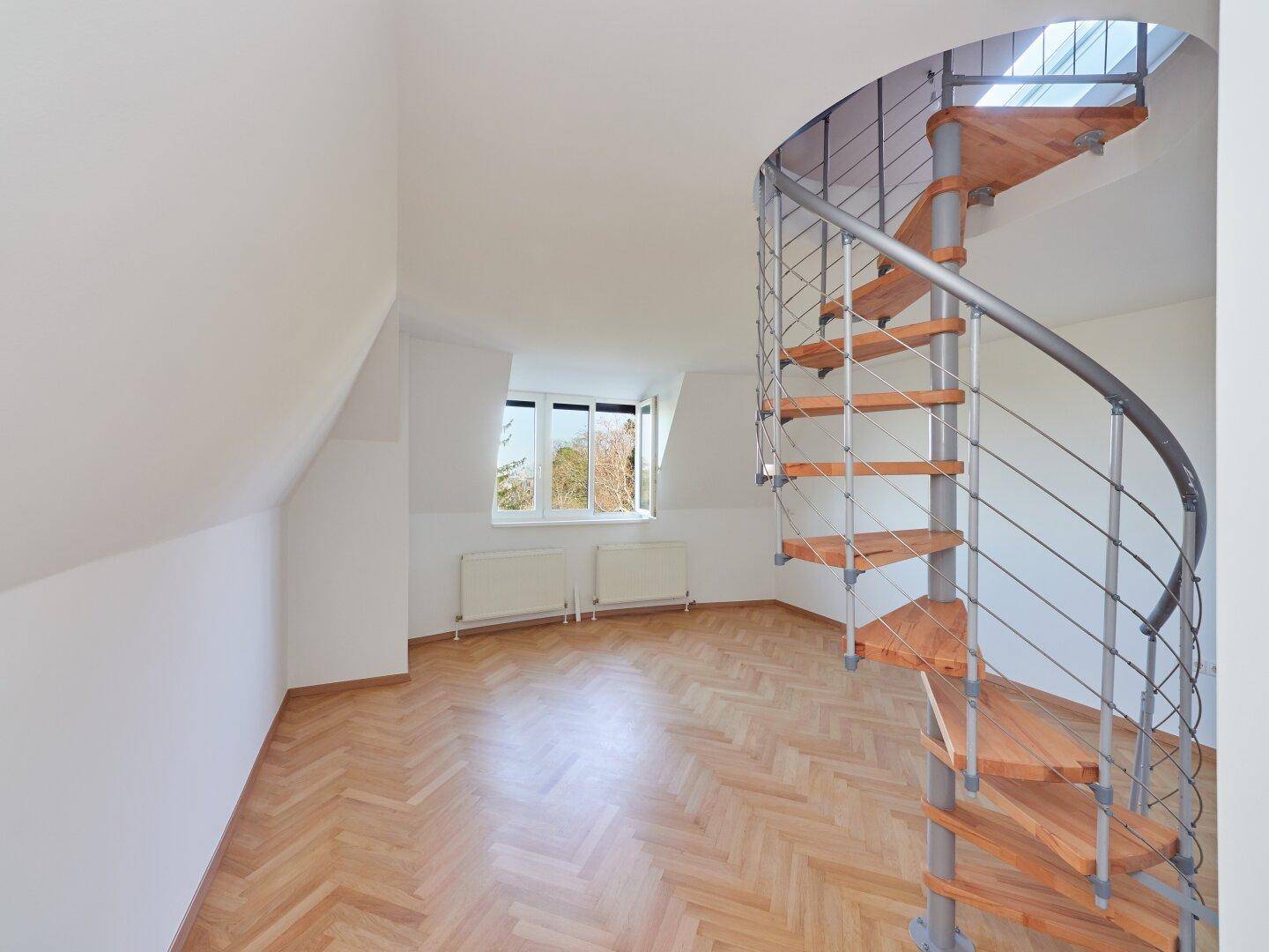 Helles Dachzimmer mit Fischgrätparkett und einer eleganten Wendeltreppe.