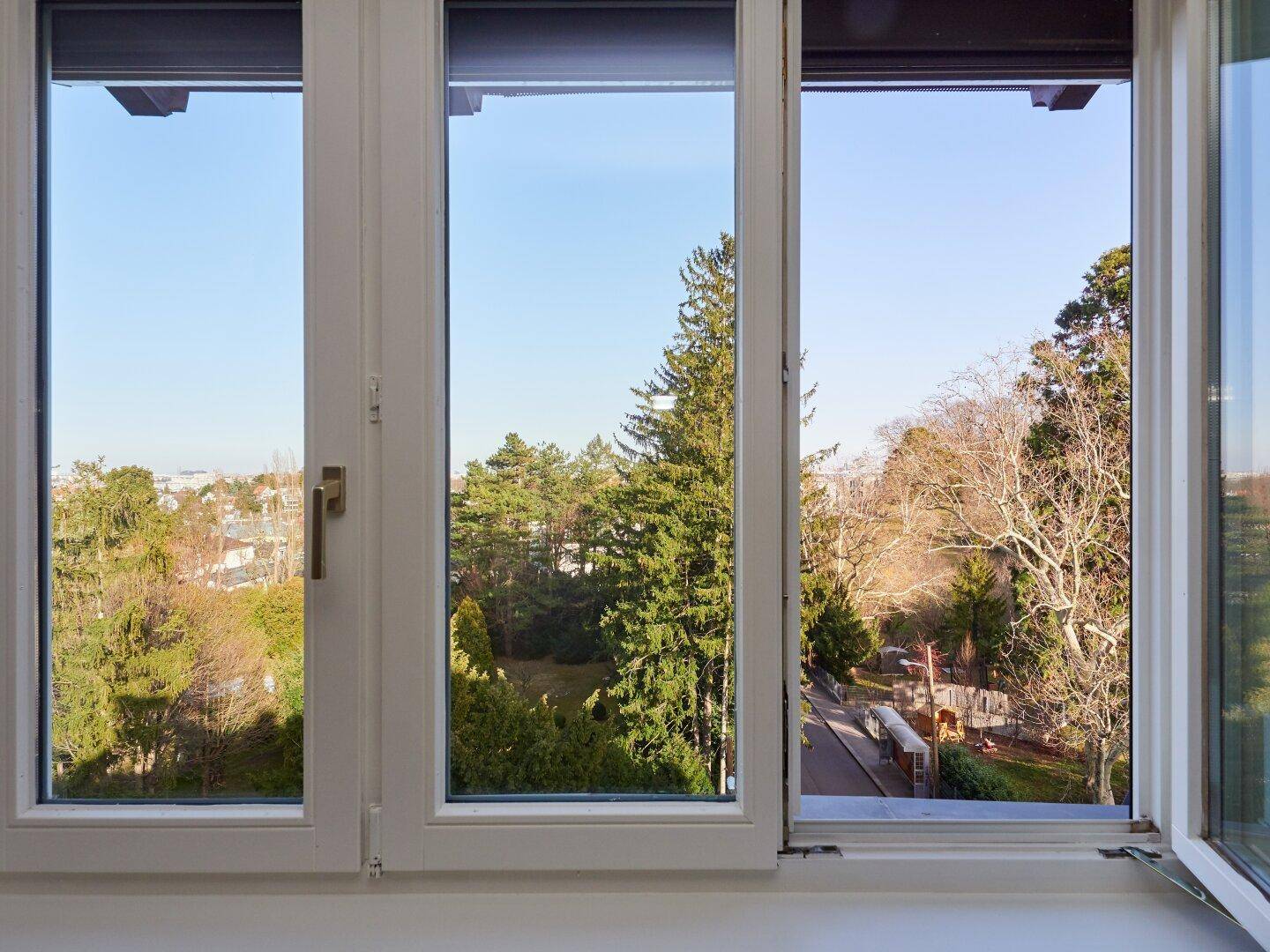 Weitläufiger Ausblick aus einem Fenster auf grüne Bäume und die Umgebung.