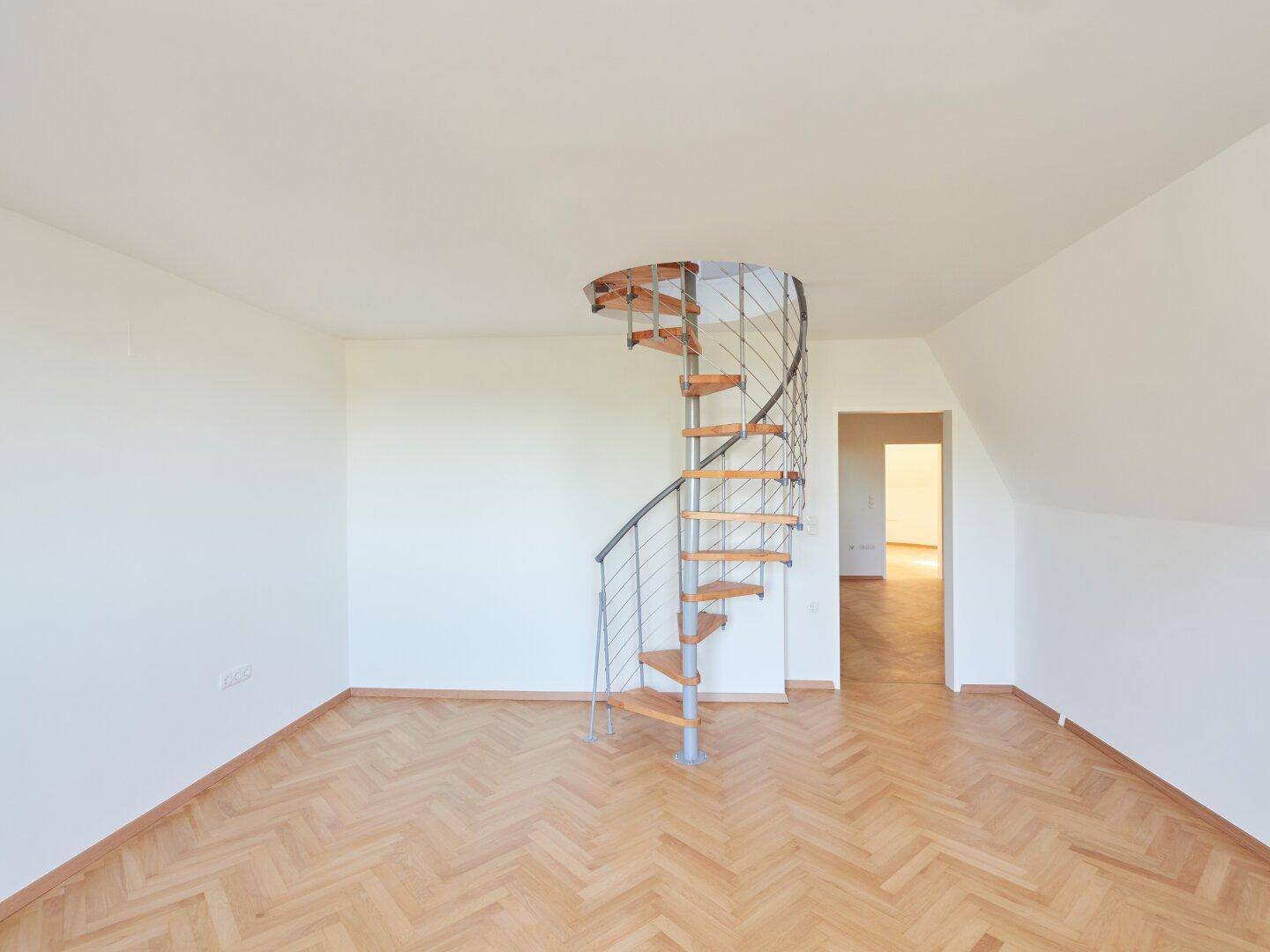 Helles Dachzimmer mit Fischgrätparkett, Dachschrägen und einer modernen Wendeltreppe.
