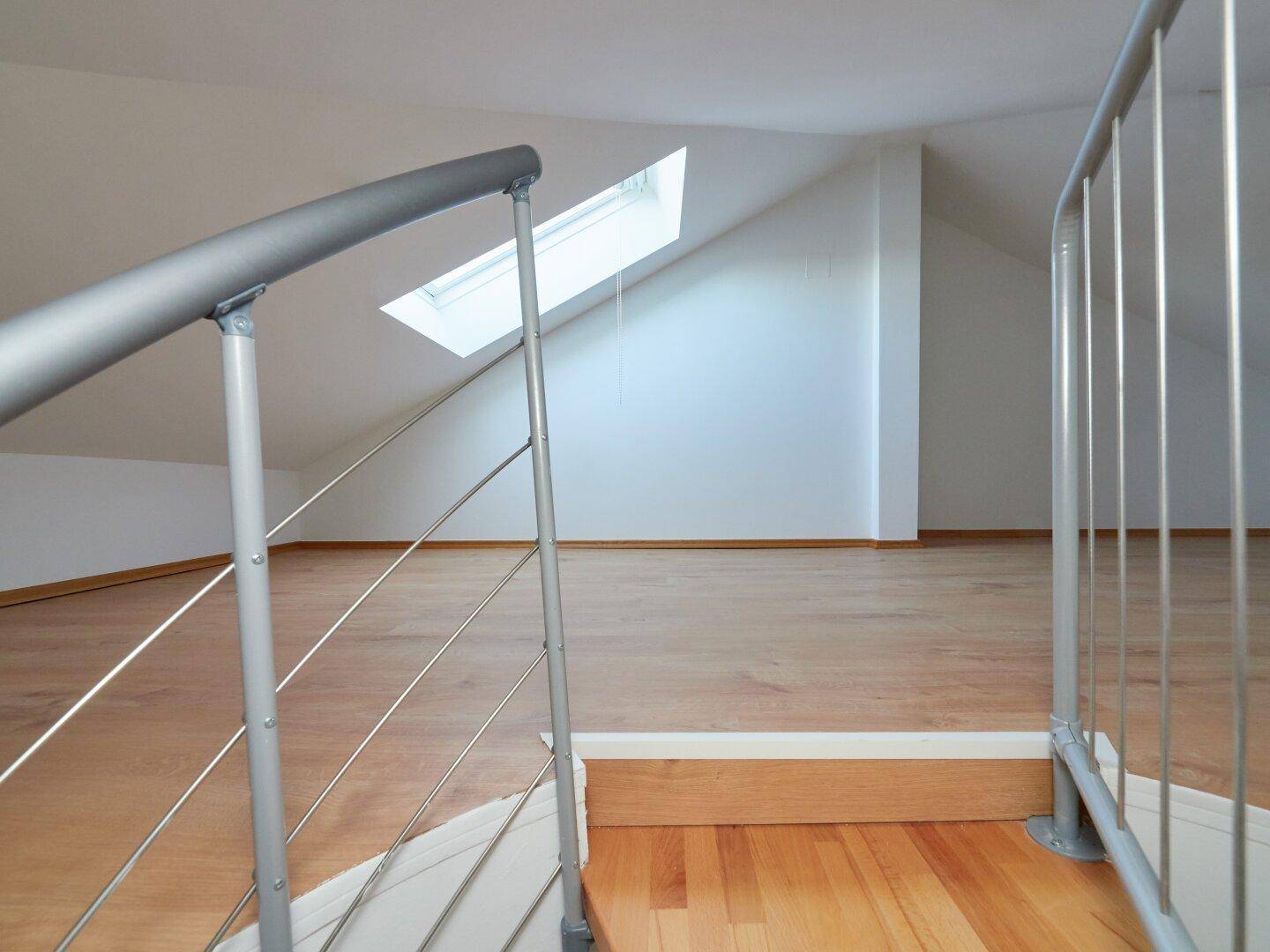 Heller Dachbodenbereich mit Laminatboden, Dachfenster und moderner Treppe.