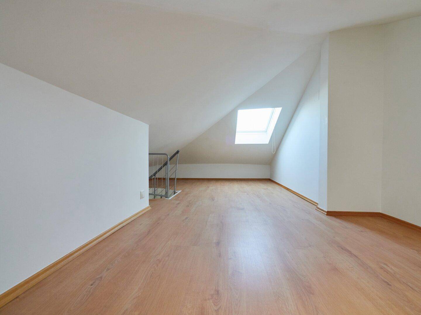Geräumiger Dachbodenbereich mit Laminatboden, Dachschrägen und einem Dachfenster.